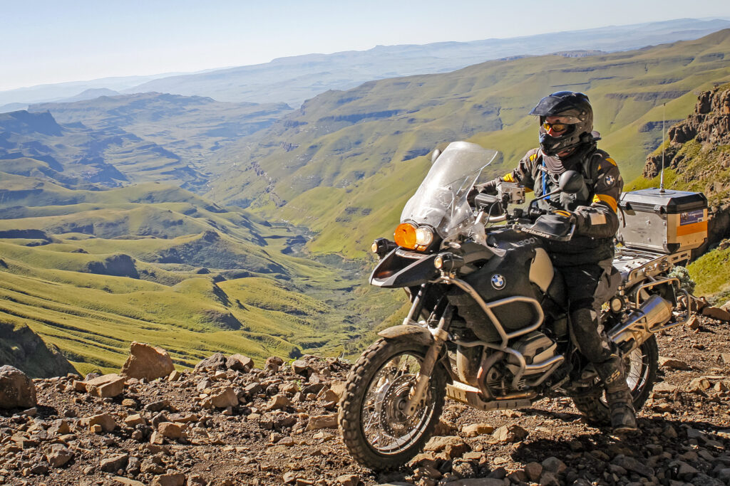 Adventure motorcycle rider overlooking a dramatic mountain valley during an off-road expedition.